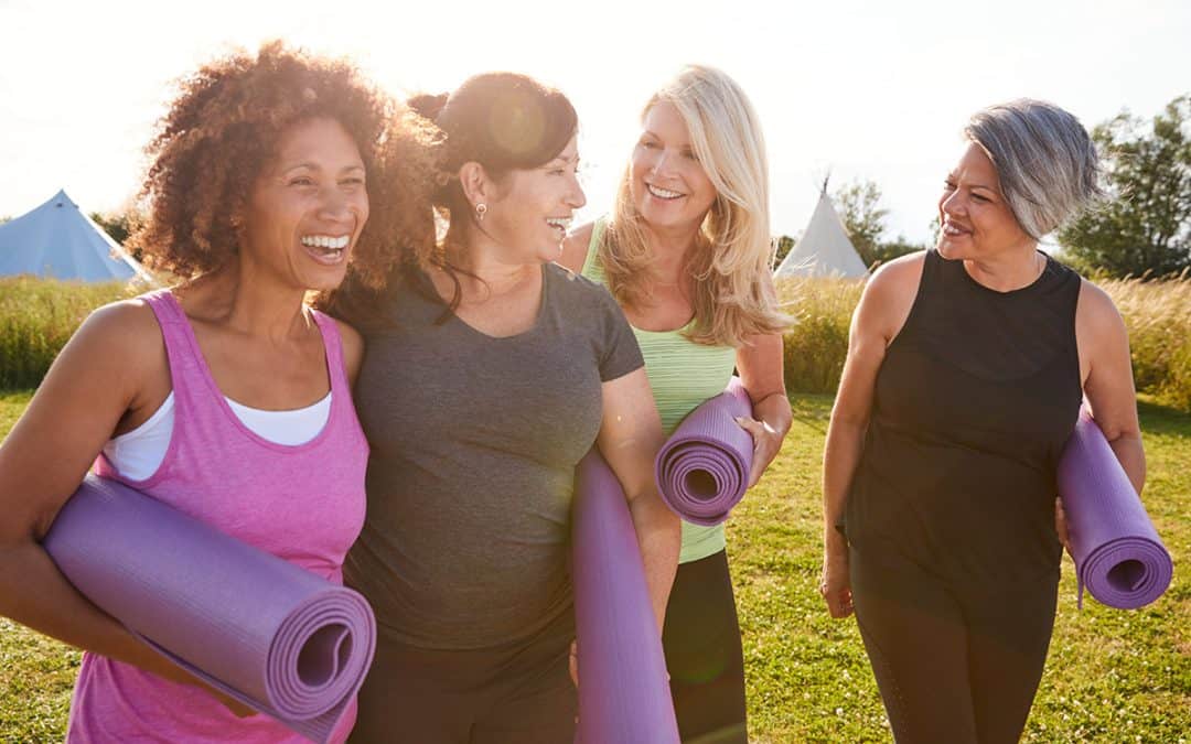 Happy and healthy ladies walking together holding yoga mats.